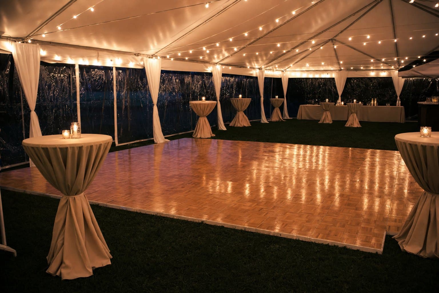 Parquet dance floor under a tent with string lights and draped cocktail tables by Creative Events & Rentals