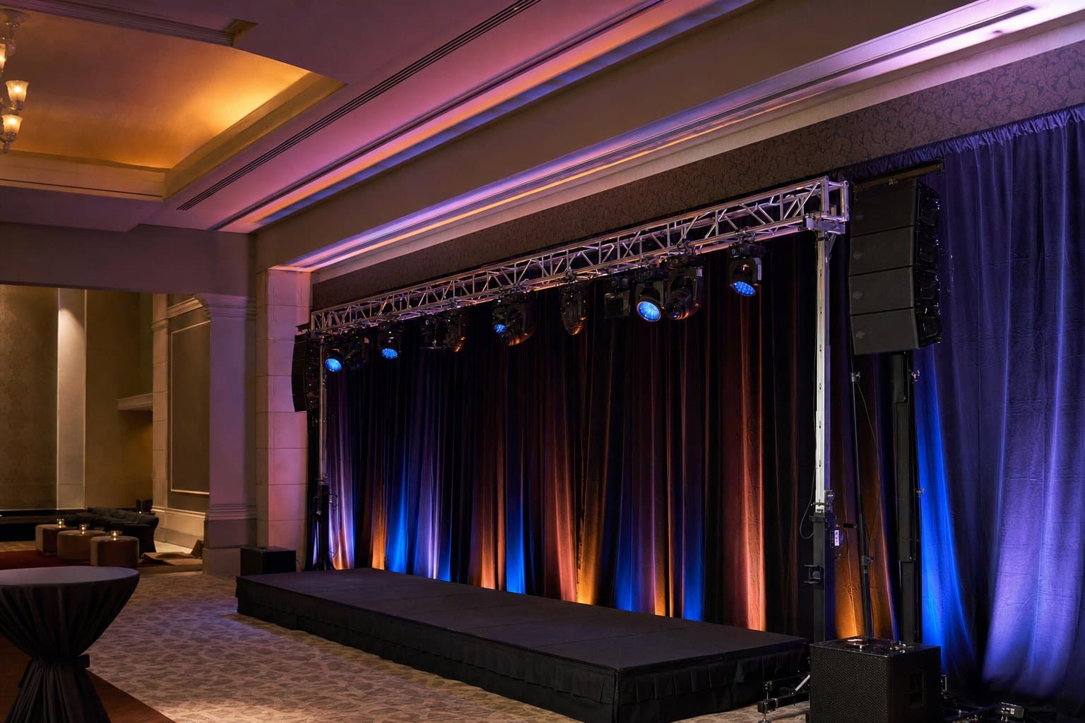 Event staging platform with overhead lighting truss, stage uplighting and a line-array speaker by Creative Events & Rentals